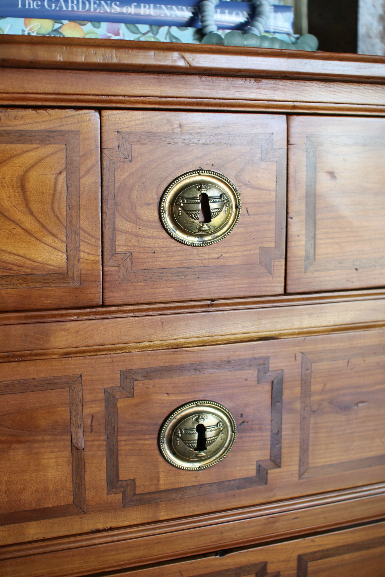 Close-up of a wooden chest of drawers with two visible drawers, featuring brass oval handles and decorative inlay panels.
