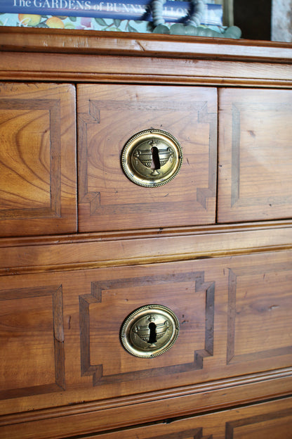 Close-up of a wooden chest of drawers with two visible drawers, featuring brass oval handles and decorative inlay panels.