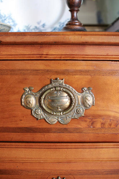 Close-up of a vintage ornate brass drawer pull handle on a warm brown wooden chest or cabinet.